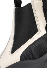 Svart och krämfärgad ankelsko med en slät läder- och strukturerad gummiyta, elastisk sidopanel och kontrasterande sömdetalj.