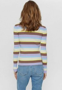Donna con capelli castani alla spalla che indossa un maglione a coste aderente con strisce orizzontali pastello e jeans azzurri chiari, vista da dietro.