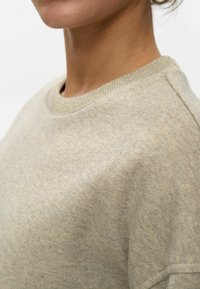 Sudadera de color beige claro con una superficie texturizada y cuello acanalado. La tela tiene un brillo sutil y parece suave y cómoda.