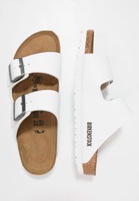 Sandali Birkenstock bianchi con due cinturini regolabili, fibbie argentate, soletta in sughero e suola in gomma testurizzata. Taglia 37 segnata all'interno.