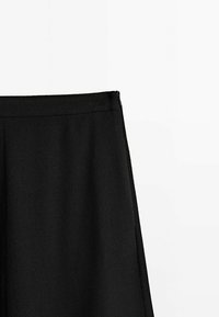 Jupe noire taille haute avec détail de fermeture éclair latérale, texture de tissu lisse, présentée sur un fond blanc uni.