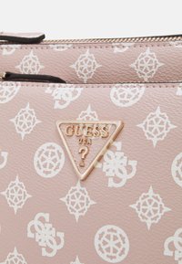 Borsa sintetica texturizzata rosa con motivi a logo bianchi. Include un badge triangolare dorato di Guess USA con un punto interrogativo. Chiusura a zip.