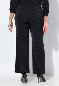 Pantaloni neri con pois bianchi, design a gamba larga, vita elastica, tessuto morbido, indossati con scarpe con tacco alto nere.