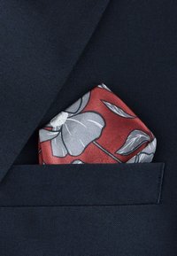 Rotes florales Einstecktuch mit grauen Akzenten, ordentlich gefaltet in einer dunkelblauen Sakkotasche aus strukturiertem Stoff.