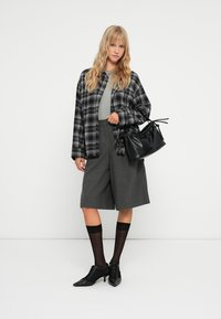 Chemise oversize à carreaux noir et blanc, T-shirt gris, shorts plissés gris, sac à main noir, chaussettes noires et chaussures à lacets.