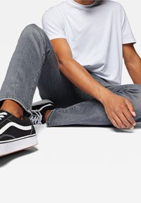 Jeans de mezclilla gris, camiseta de algodón blanca y zapatillas negras con acentos blancos, en una pose sentada que muestra un ajuste casual y relajado, así como la textura.