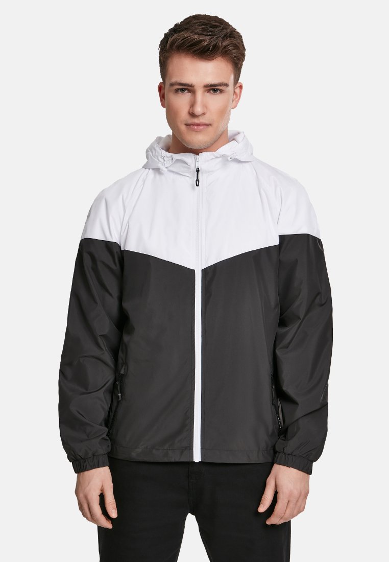 Veste coupe-vent noir et blanc avec capuche, fermeture éclair frontale et design coloré avec texture lisse et poignets élastiques.