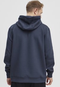 Tumši jūras spēka krāsas kapucīte ar vienkāršu dizainu. Izgatavota no mīksta auduma, ar lielu kapuci un ribotiem manžetēm un apakšdaļu.