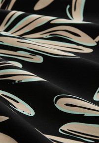 Schwarzer Stoff mit einem fließenden, abstrakten Muster in hellem Beige und Teal. Die Textur wirkt glatt, mit sanften Falten, die sichtbar sind.