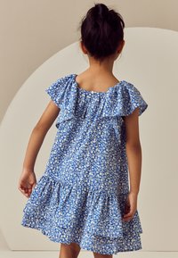 Robe fleurie bleue avec manches à volants, dotée d'un ourlet en plusieurs couches et d'une fermeture à boutons dans le dos, confectionnée en tissu léger.