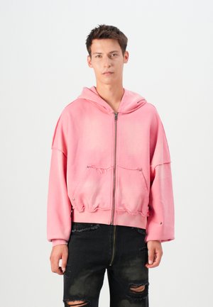 Un hoodie court rose avec une fermeture éclair à l'avant, une capuche, un ourlet déchiré et deux poches avant. Assorti avec un jean noir déchiré.