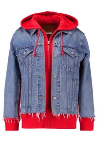 Denimjacka i blått med fransad fåll och två bröstfickor, lagd över en röd hoodie med dragsko och dragkedja.