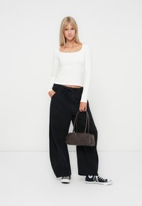Long-sleeved white crop top and black wide-leg pants, paired with a dark handbag and black sneakers with white accents. Smooth texture.