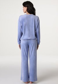 Completo pigiama in velluto blu, composto da una maglietta a maniche lunghe a vestibilità ampia e pantaloni a gamba larga. Tessuto morbido e leggera variazione di colore.