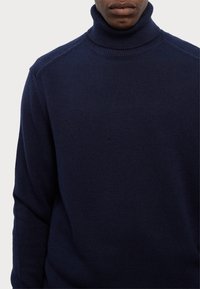 Maglione a collo alto blu navy realizzato in tessuto lavorato a maglia, con un colletto a coste e una superficie testurizzata, maniche lunghe e una vestibilità morbida.