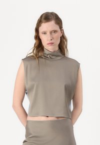 Gekürztes ärmelloses Oberteil in Taupe, mit hohem Halsauschnitt und glattem, elastischem Stoff. Akzentuiert mit einem klaren, schlichten Schnitt.
