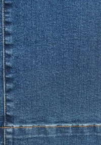 Primo piano di un tessuto in denim blu con dettagli di cuciture arancioni verticali e orizzontali.