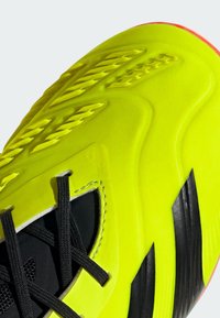 Baskets de sport jaune vif avec un dessus en synthétique texturé, des accents noirs et un système de laçage intégré. Présente un design incurvé et une semelle rouge.