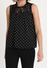 Top senza maniche nero con accento in pizzo e pois bianchi, caratterizzato da un design plissettato e una scollatura rotonda.