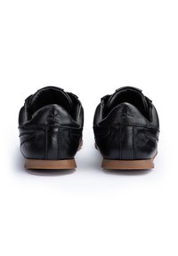 Para czarnych skórzanych butów casualowych z brązowymi podeszwami, widziana od tyłu na białym tle.