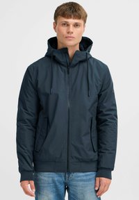 Chaqueta con capucha color marino, con cierre frontal, bolsillos laterales, puños elásticos y un material suave y ligero. Incluye cordones ajustables.