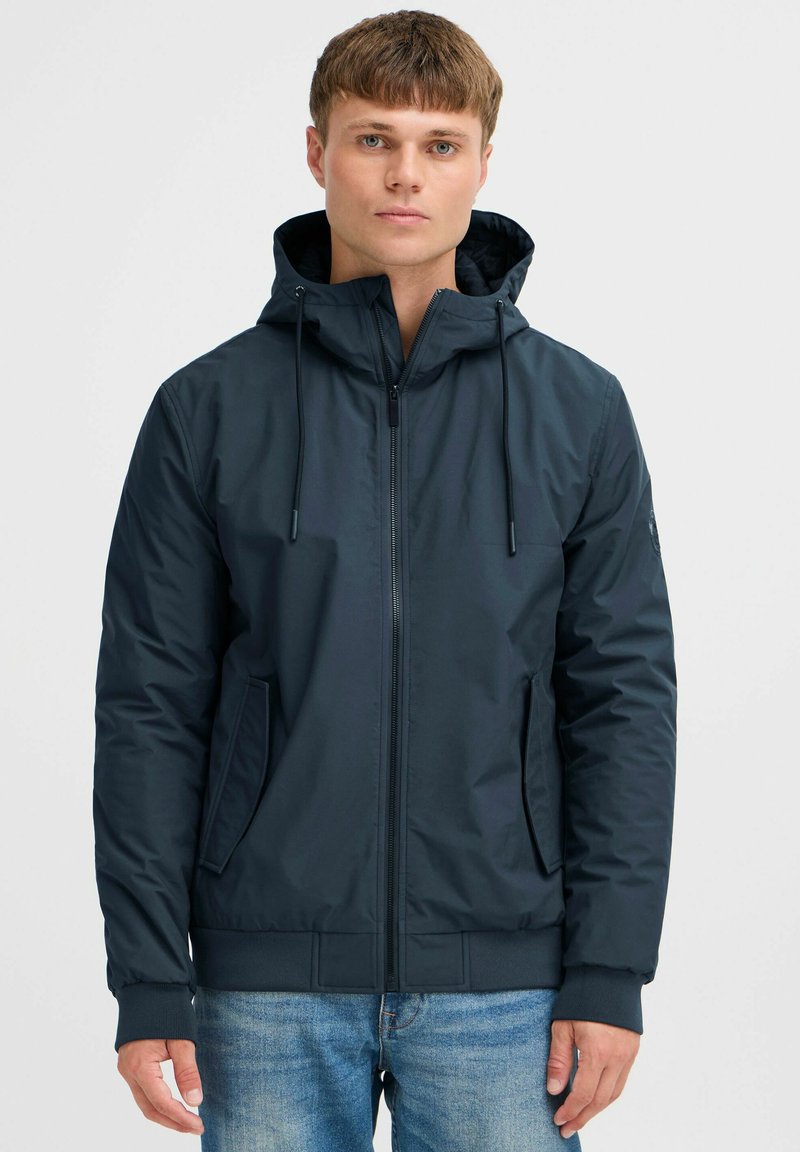 Chaqueta con capucha color marino, con cierre frontal, bolsillos laterales, puños elásticos y un material suave y ligero. Incluye cordones ajustables.