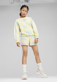 Felpa chiara e pantaloni corti con motivo floreale in giallo, blu e rosa. Indossati con calze bianche e sneaker beige.