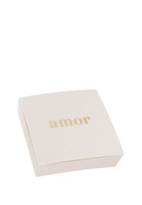 Kwadratowe, bladoróżowe pudełko o gładkiej powierzchni. Na górnej powierzchni, na środku, znajduje się słowo "amor" w kolorze złotym. Minimalistyczny design.
