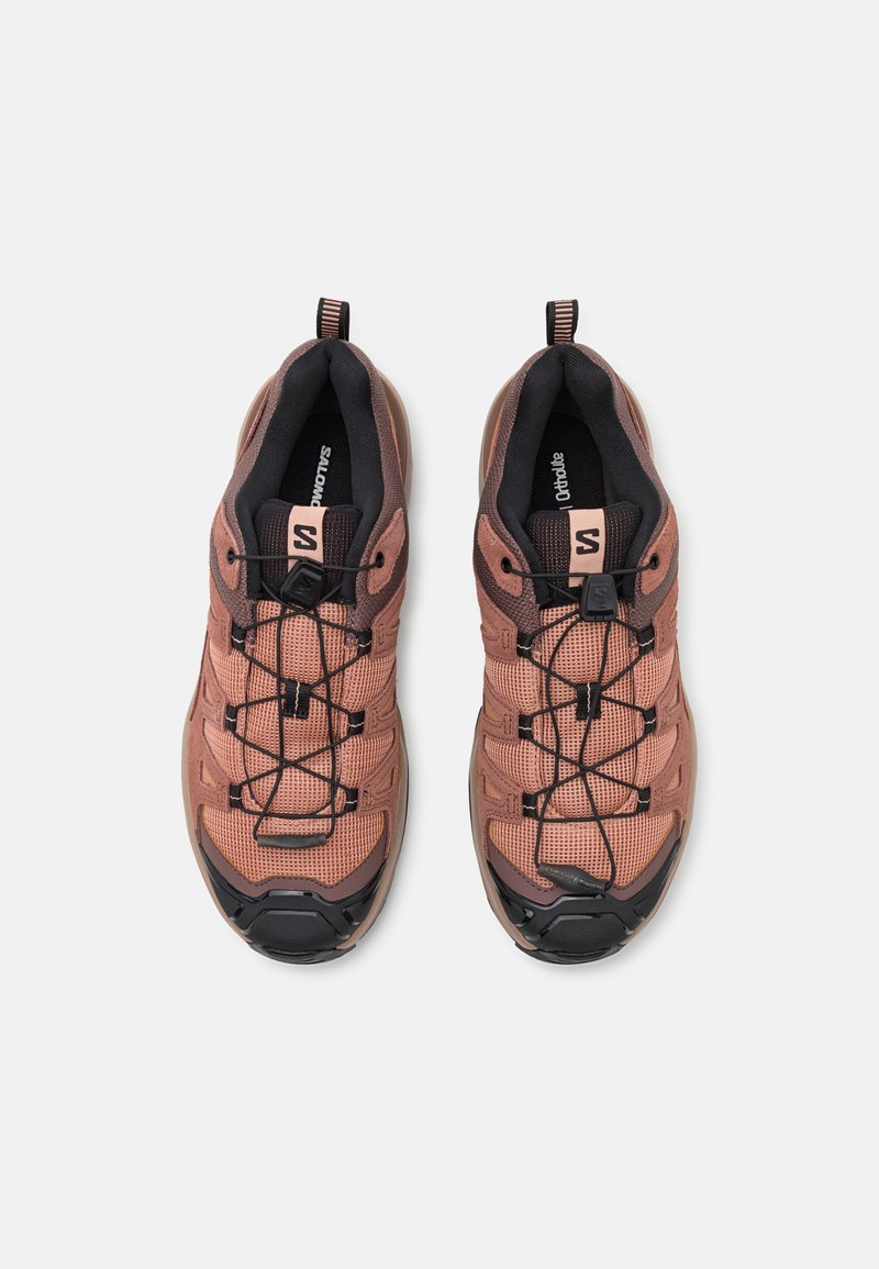 Buty sportowe z siateczkową cholewką w jasnoróżowym odcieniu, czarnymi akcentami i elastycznym systemem sznurowania; wzmocniony przód i wyściełany kołnierz.