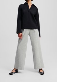 Top negro de estilo polo, pantalones anchos grises y zapatos planos negros con lunares blancos. La parte superior cuenta con una tapeta y mangas largas.