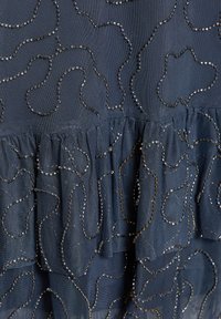 Tissu bleu foncé avec des couches froncées, décoré de petites perles noires brillantes formant des motifs de lignes ondulées irrégulières.