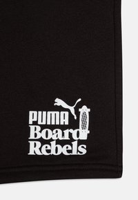 Tissu noir avec du texte blanc qui indique "PUMA Board Rebels" accompagné d'un logo d'un puma en saut et d'un graphique de skateboard.