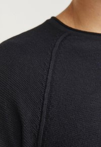 Suéter de punto azul marino con tejido texturizado, presenta un cuello redondo y un sutil detalle de costura en los hombros. Material lavable a máquina.