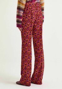 Pantalon coloré à motifs avec des rectangles arrondis en rose, orange et rouge. Fabriqué dans un tissu doux et lisse avec une coupe évasée au niveau des jambes.