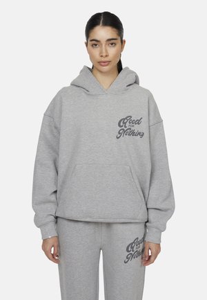 Un hoodie gris court en tissu doux avec une grande poche frontale, arborant un logo imprimé sur le côté gauche. Associé à un pantalon de survêtement gris assorti.