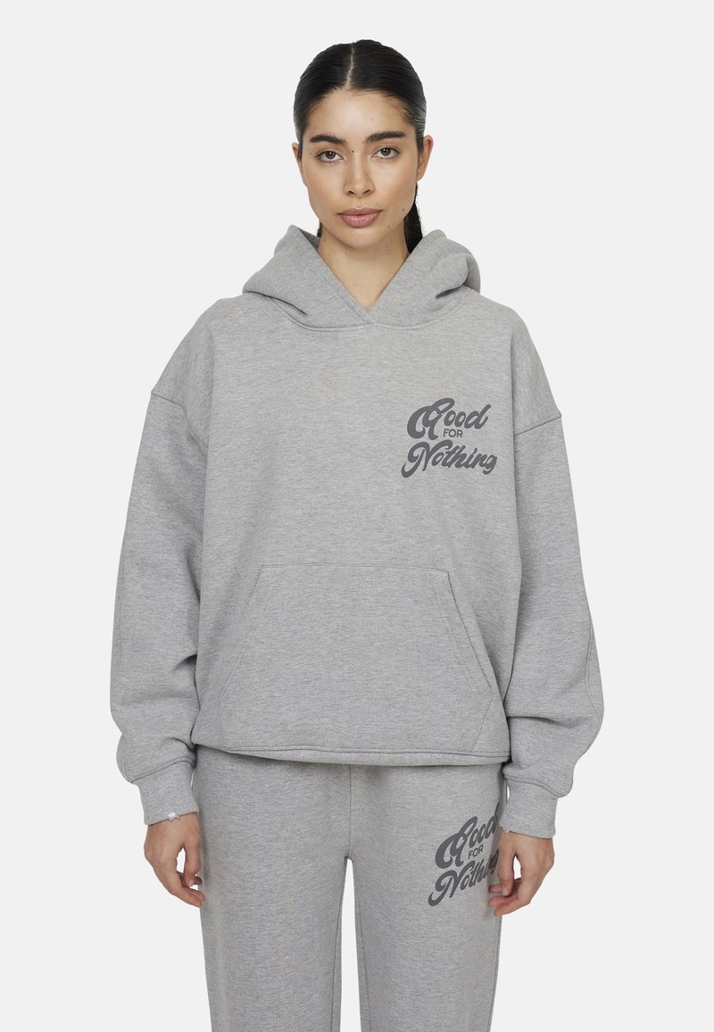 Felpa con cappuccio grigia tagliata in tessuto morbido, con una grande tasca frontale e un logo stampato sul lato sinistro. Abbinata a pantaloni da tuta grigi coordinati.