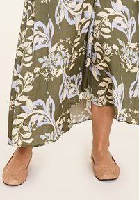 Blumenkleider im Maxi-Stil in Olivgrün mit blauen und weißen Mustern. Braune Slipper mit strukturierter Oberfläche.