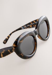Round, oversized sunglasses with a tortoiseshell pattern, glossy black frame, and dark lenses; made from lightweight plastic material.