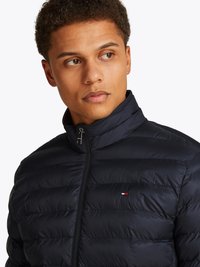 Navy puffer jacket with quilted design, high collar, full zipper, and branded logo accent. Made from a smooth, lightweight material.