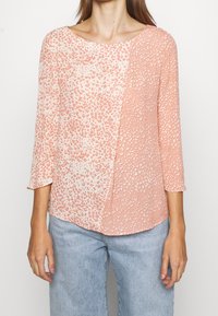 Sudadera de manga larga con un diseño bicolor que presenta un patrón texturizado de durazno sobre crema. Cuello redondeado y corte relajado. Tela suave.