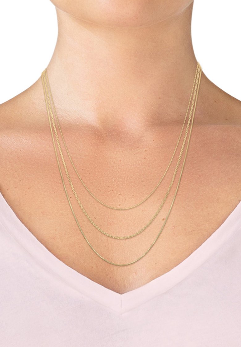 Gold multi-layered necklace with three chains of varying lengths, featuring smooth and twisted textures, resting on a pale neckline.