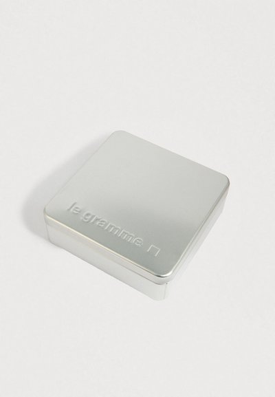 Mali srebrni metalni limenik s utisnutim tekstom "le gramme" i kvadratnim logotipom na poklopcu, postavljen na bijelu površinu.