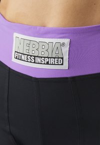 Leggings de fitness pretos com uma larga cinta roxa. Apresenta um rótulo branco proeminente que diz "NEBBIA FITNESS INSPIRED". Textura suave.