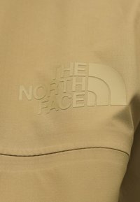 Μπεζ ύφασμα με ανάγλυφο σχέδιο λογότυπου «THE NORTH FACE» και γραφικό μισού θόλου, που δίνει έμφαση στην υφή και τις λεπτομέρειες του branding.