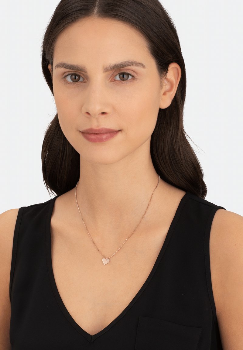 Roze gouden harthanger ketting op een fijne ketting, gedragen over een zwart V-hals shirt. Gladde textuur met minimalistische ontwerpelementen.