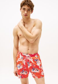 Costume de baie roșii cu flori, cu talie ajustabilă, având un model vibrant de flori albe și albastre, realizat dintr-un material ușor și cu uscare rapidă.