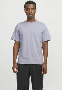 Camiseta de algodón de color púrpura claro con cuello redondo, mangas cortas y corte relajado, combinada con pantalones negros. Textura suave, diseño minimalista.