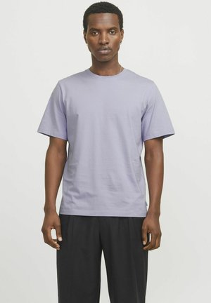 Camiseta de algodón de color púrpura claro con cuello redondo, mangas cortas y corte relajado, combinada con pantalones negros. Textura suave, diseño minimalista.