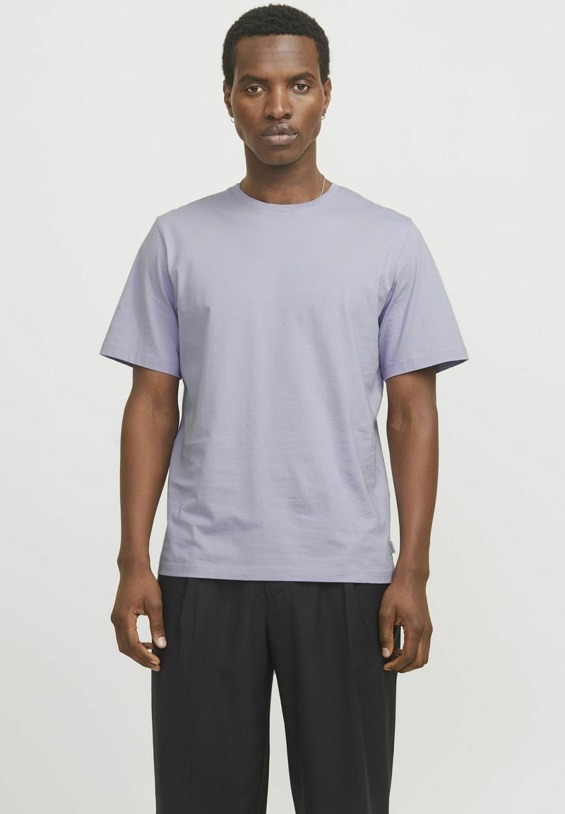 Camiseta de algodón de color púrpura claro con cuello redondo, mangas cortas y corte relajado, combinada con pantalones negros. Textura suave, diseño minimalista.