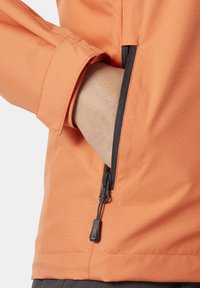 Oranje jack met een ritszak op de mouw, die de gladde stoftextuur toont en zwarte ritshardware voor contrast.